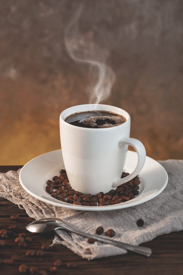 Eine Tasse Kaffee auf einem Teller mit Bohnen und einem Löffel Eine Tasse Kaffee auf einem Teller mit Bohnen und einem Löffel